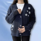Person wearing a dark blue cable knit cardigan with star patterns on a light blue background